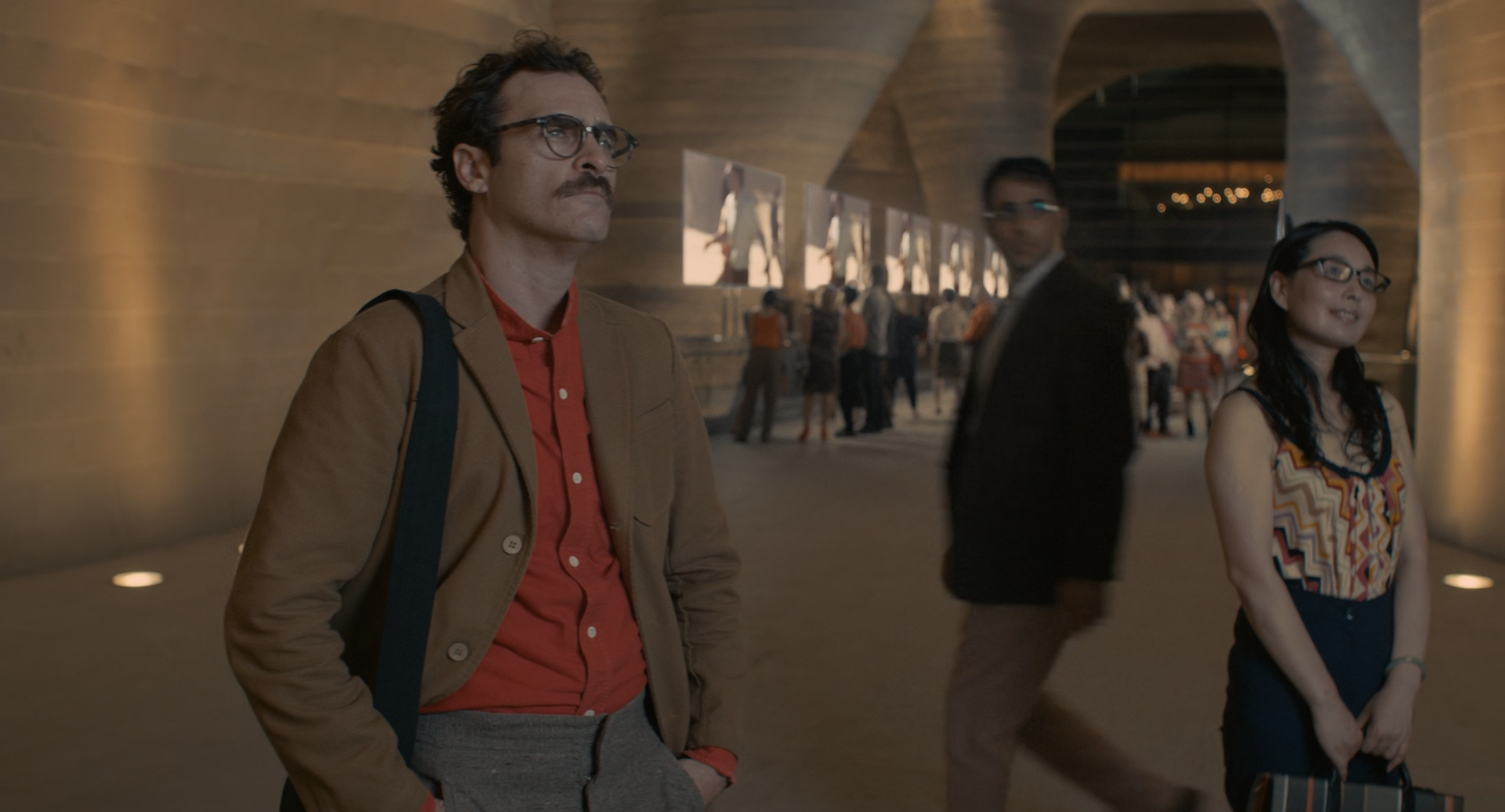 Her screenshot, Theo and extras gazing into an advertisement, wearing high-waisted pants